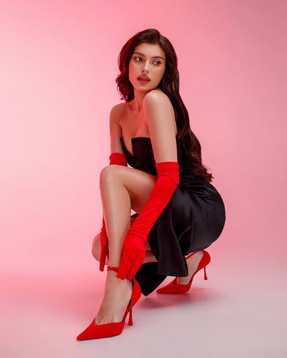 Woman in a black dress with red gloves and shoes on a pink background