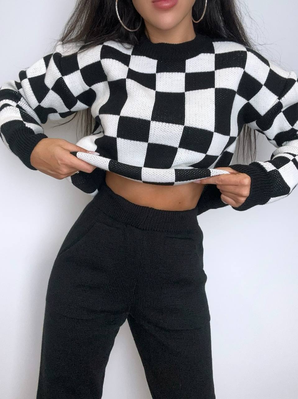 Person wearing a black and white checkered sweater and black pants against a white background