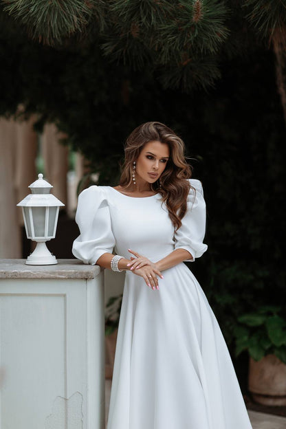Woman in a white dress standing outdoors with greenery in the background
