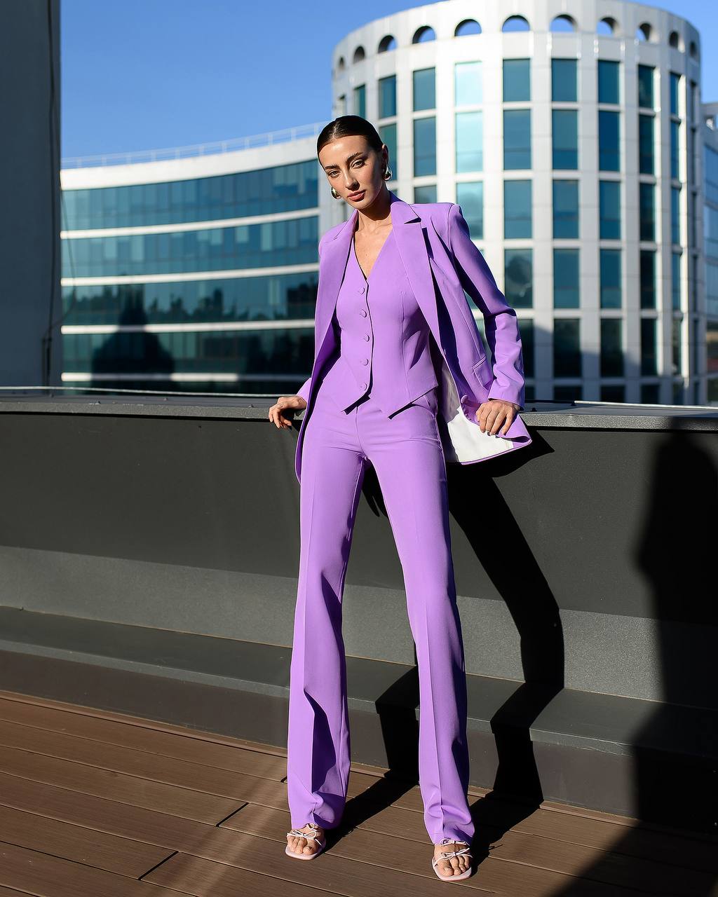 Woman in a purple suit standing on a rooftop with modern building in the background