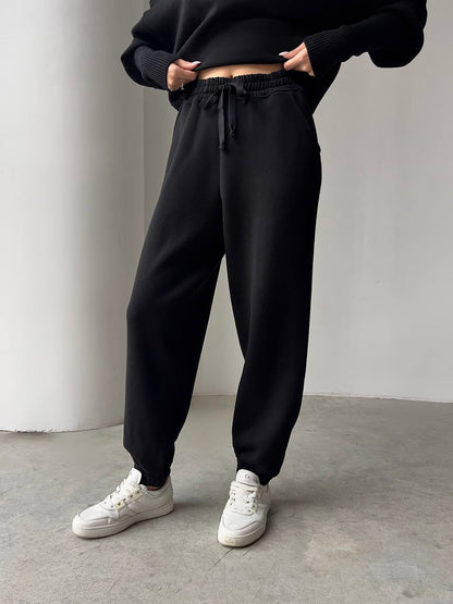 Person wearing black jogger pants and white sneakers on a plain background