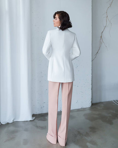 Person wearing a white coat and pink pants against a plain background