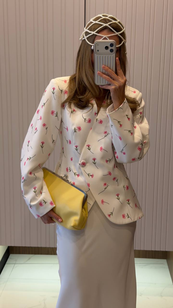 Person wearing a floral blouse and holding a yellow clutch in front of a mirror.