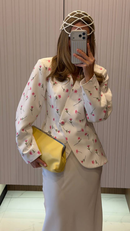 Person wearing a floral blouse and holding a yellow clutch in front of a mirror.