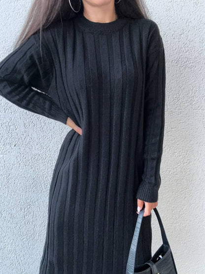 Person wearing a long black ribbed dress against a light gray background