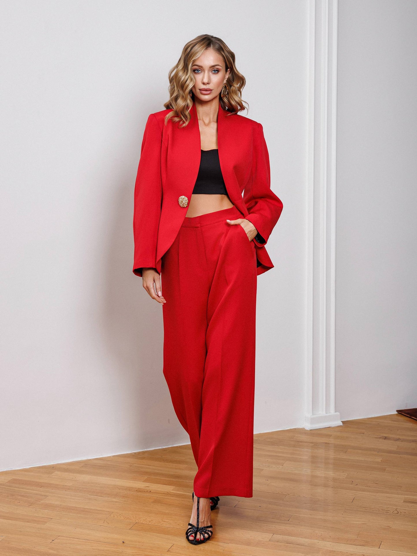 Woman wearing a red suit standing in a room with wooden floor and white walls.