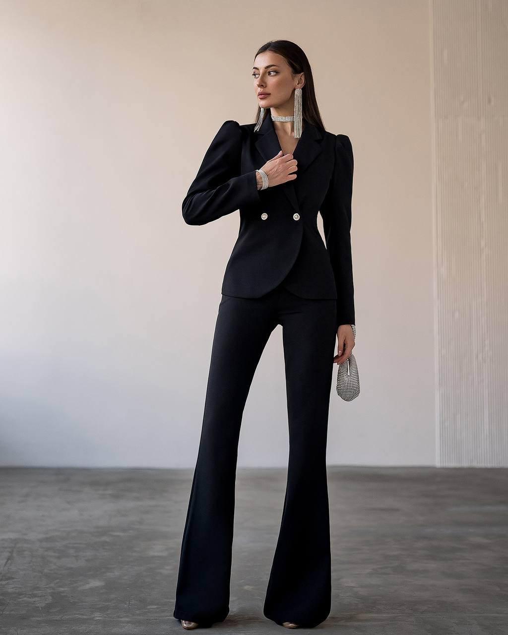 Woman wearing a black suit with flared pants against a neutral background