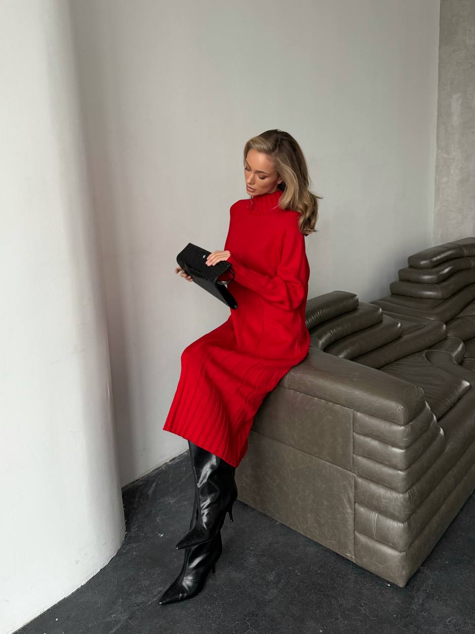 Woman in a red coat and black boots sitting on a gray bench.