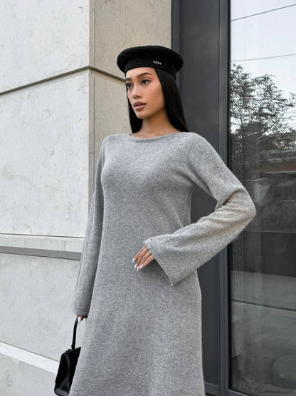 Woman wearing a gray dress and black beret standing against a modern building.