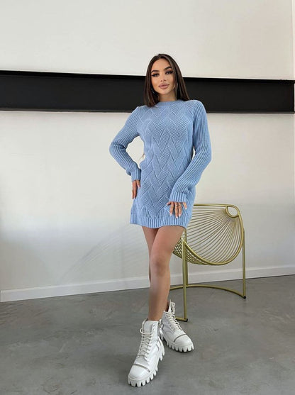 Woman wearing a blue knitted dress with white boots standing in a minimalistic room.