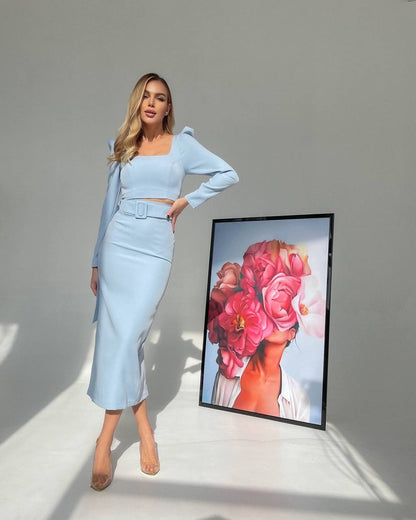 Woman in light blue outfit standing next to a framed artwork of a woman with flowers.
