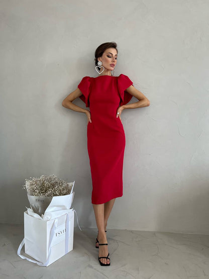 Woman in a red dress standing next to a white bag with flowers against a plain background