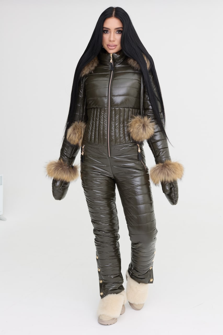 Person wearing a dark green puffer jumpsuit with fur-trimmed gloves on a white background