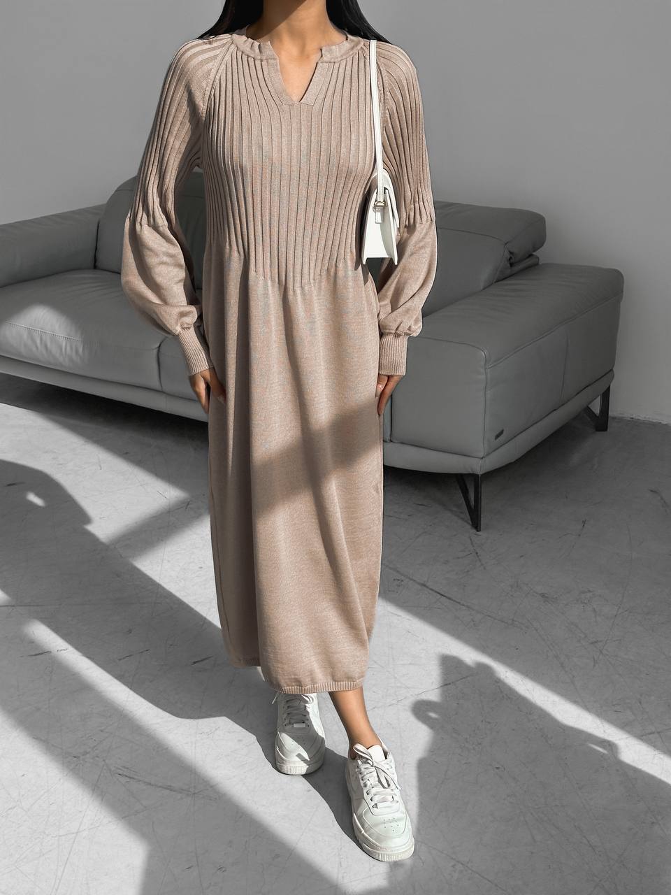 Person wearing a beige ribbed dress with white sneakers in a minimalistic room.
