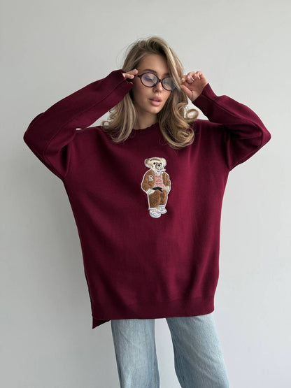 Person wearing a burgundy sweatshirt with a bear graphic on a plain background