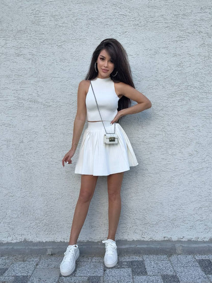 Woman in a white dress standing against a light gray wall.