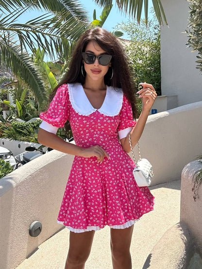 Woman in a pink dress with white collar and sleeves standing outdoors with palm trees in the background