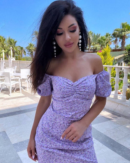 Woman wearing a purple floral dress standing outdoors with palm trees in the background