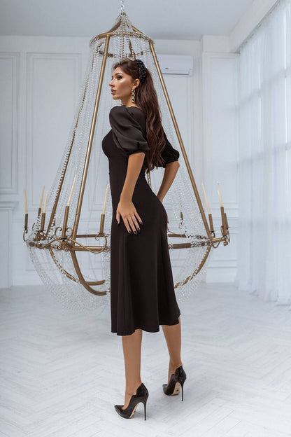 Woman in a black dress standing in a room with a large chandelier.