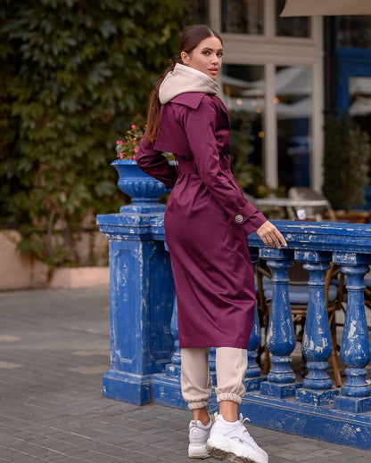 Woman in a purple trench coat standing next to a blue railing outdoors.
