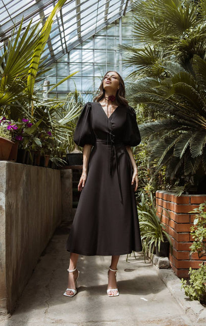 Woman in a black dress standing in a greenhouse filled with plants