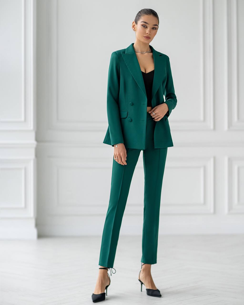 Woman wearing a green suit standing against a white paneled wall.