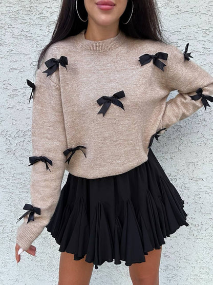 Beige sweater with black bows and a black skirt against a light gray background