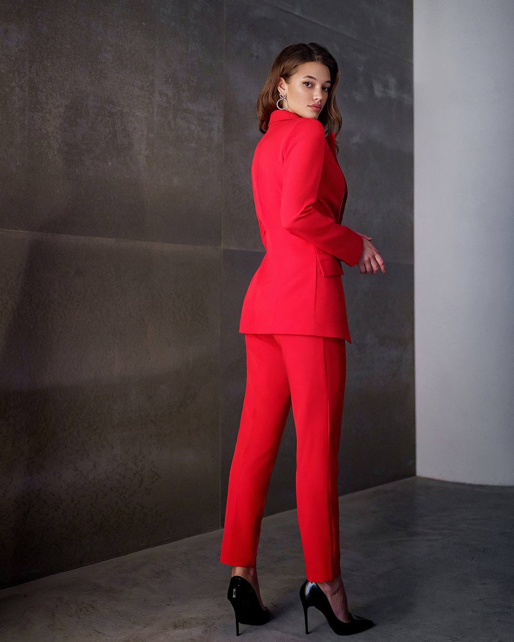 Woman wearing a red suit standing against a gray wall.