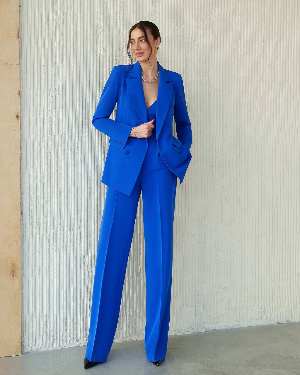 Woman wearing a blue suit standing against a textured wall.
