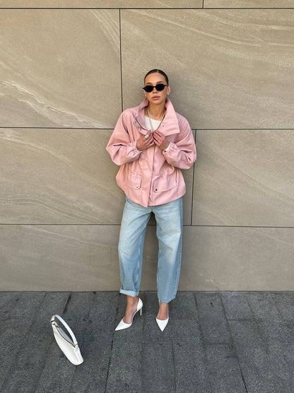 Person wearing a pink jacket and light blue jeans standing against a beige wall.