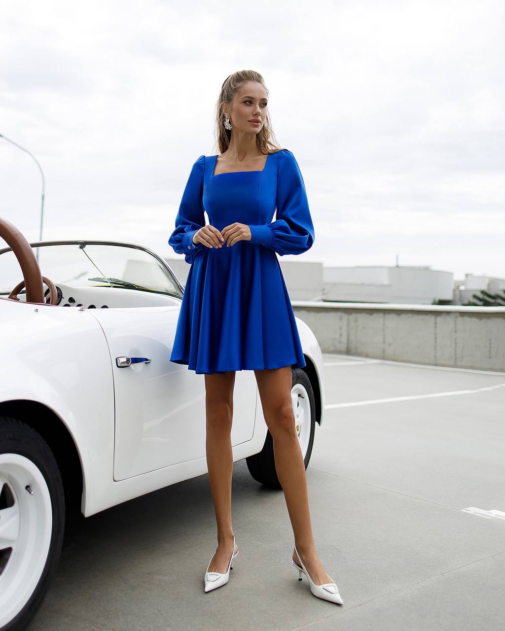 Woman in a blue dress standing next to a white car on a road.