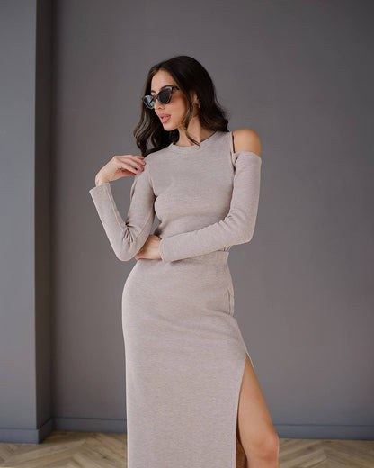 Woman wearing a gray long-sleeve dress with a slit against a plain background