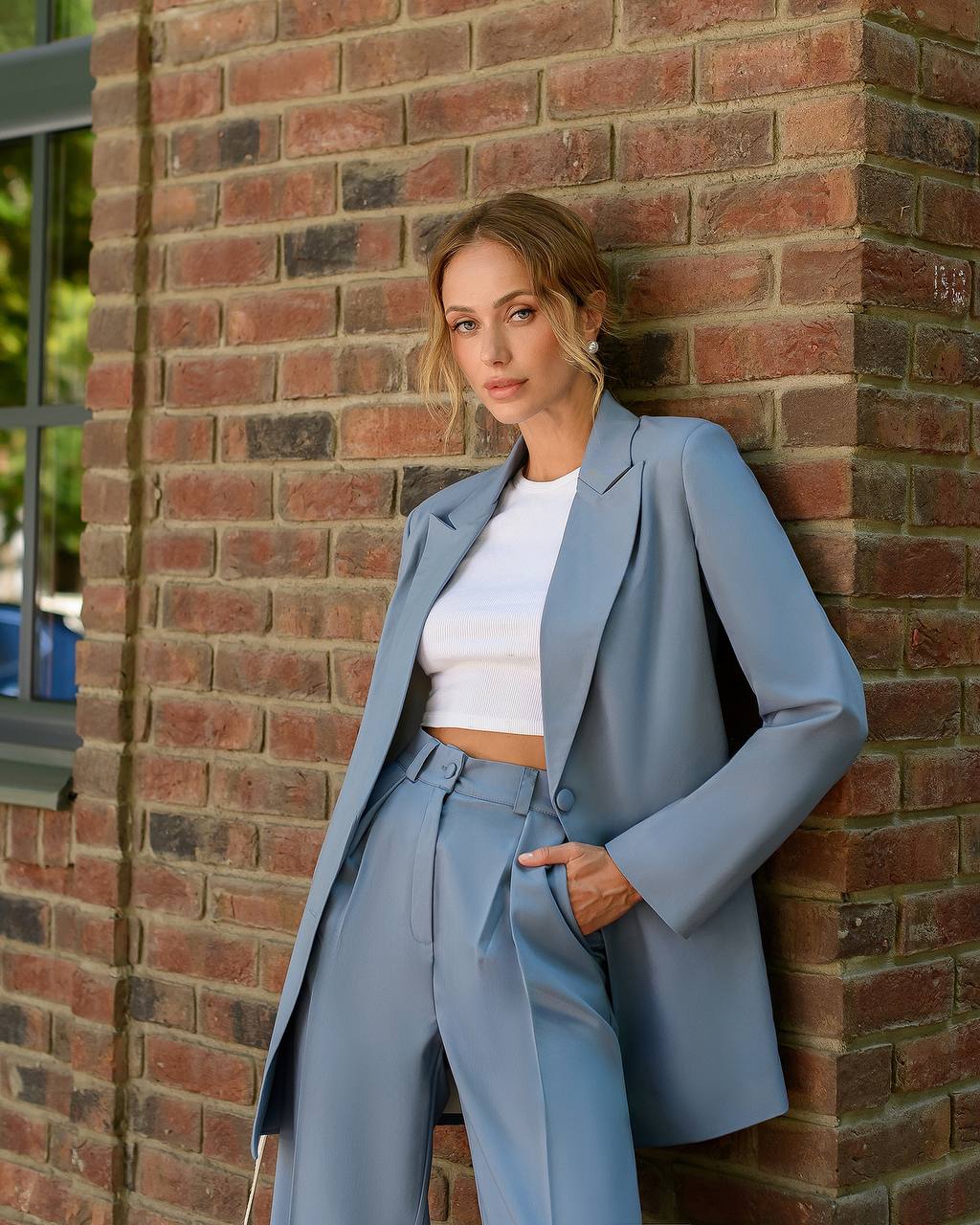 Woman in a light blue suit standing against a brick wall