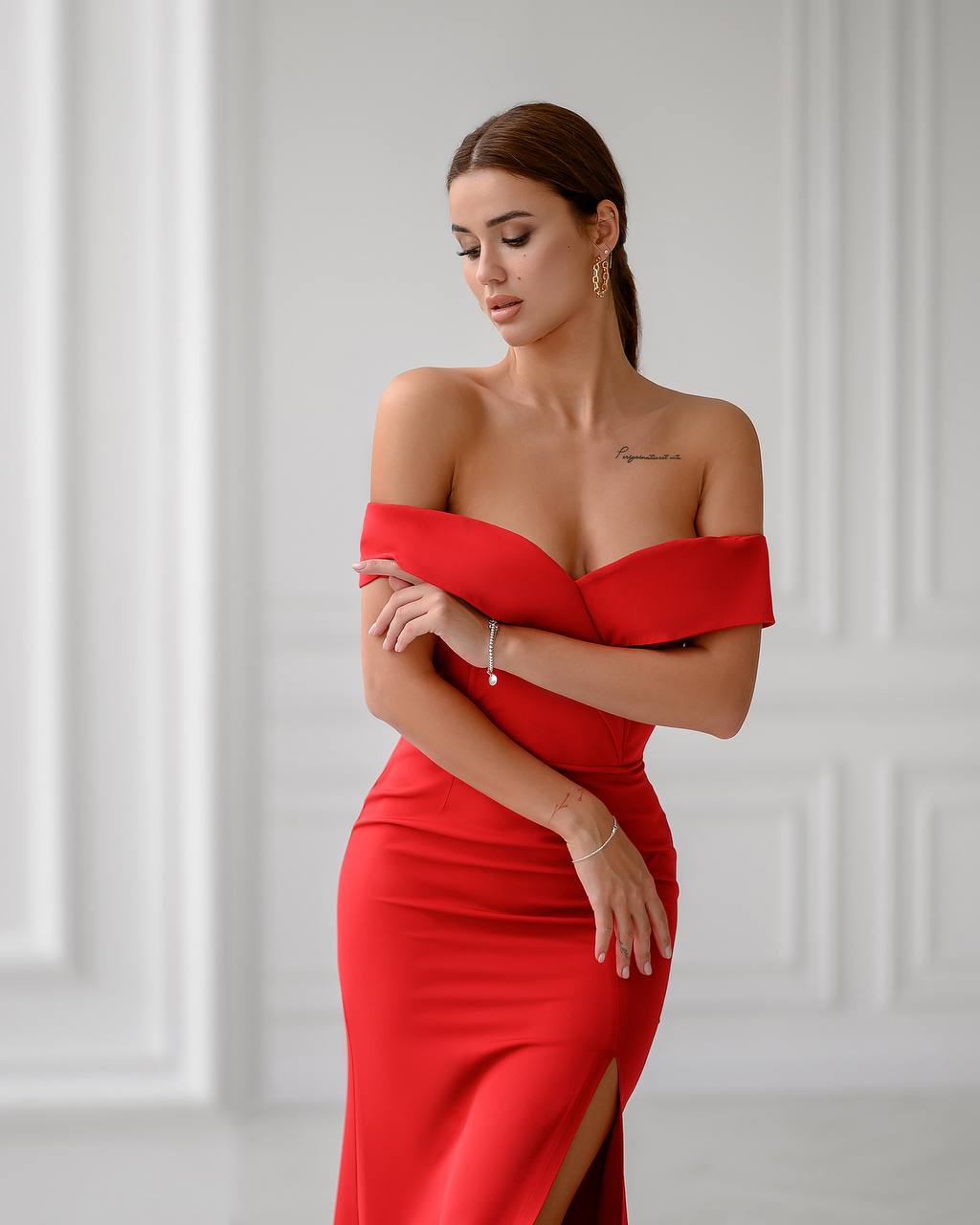 Woman wearing a red off-shoulder dress against a light gray wall.