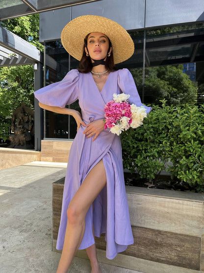 Woman in a lavender dress and straw hat holding flowers outdoors.