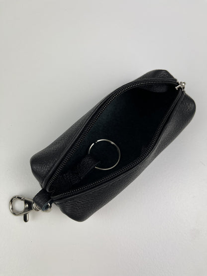 A black textured leather zippered pouch with a silver-tone metal key ring inside and a matching silver clasp on the side, shown open on a light gray background.