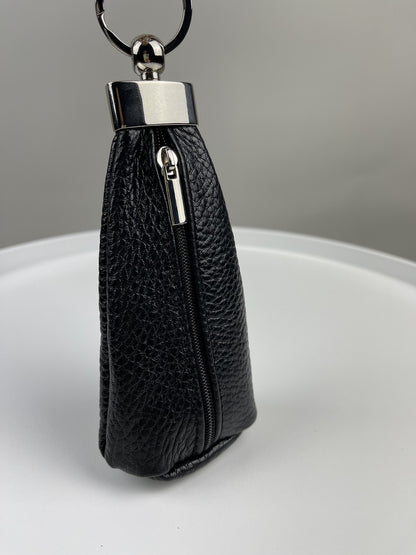 A black pebbled leather key pouch with a silver-tone metal clasp and keyring, standing upright on a white surface against a gray background.