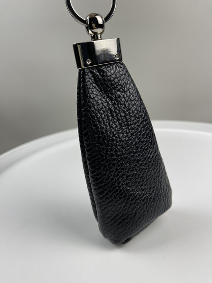 A black pebbled leather keychain pouch with a silver-tone metal clasp and split ring, standing upright on a white surface against a neutral gray background.