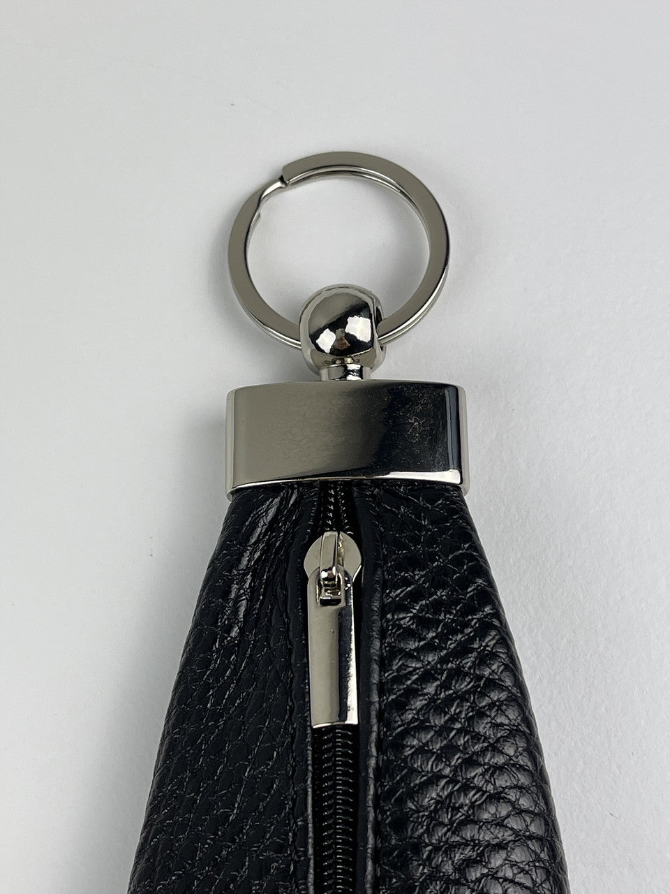A close-up of a black pebbled leather keychain or wallet attachment with a silver-tone metal split ring, cap, and zipper pull, set against a plain light gray background.