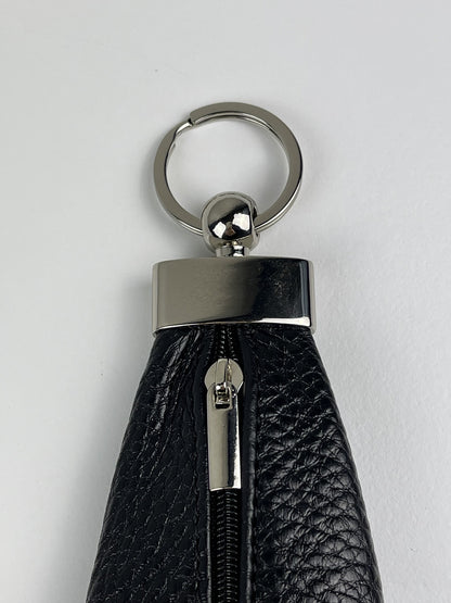 A close-up of a black pebbled leather keychain or wallet attachment with a silver-tone metal split ring, cap, and zipper pull, set against a plain light gray background.