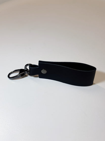 A black leather keychain strap with a black metal key ring and a silver snap button, shown on a plain light background.