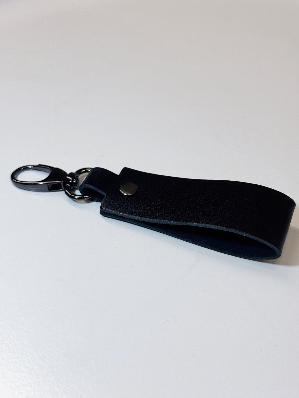 A black leather keychain strap with a black metal key ring and a silver snap button, shown on a plain white background.