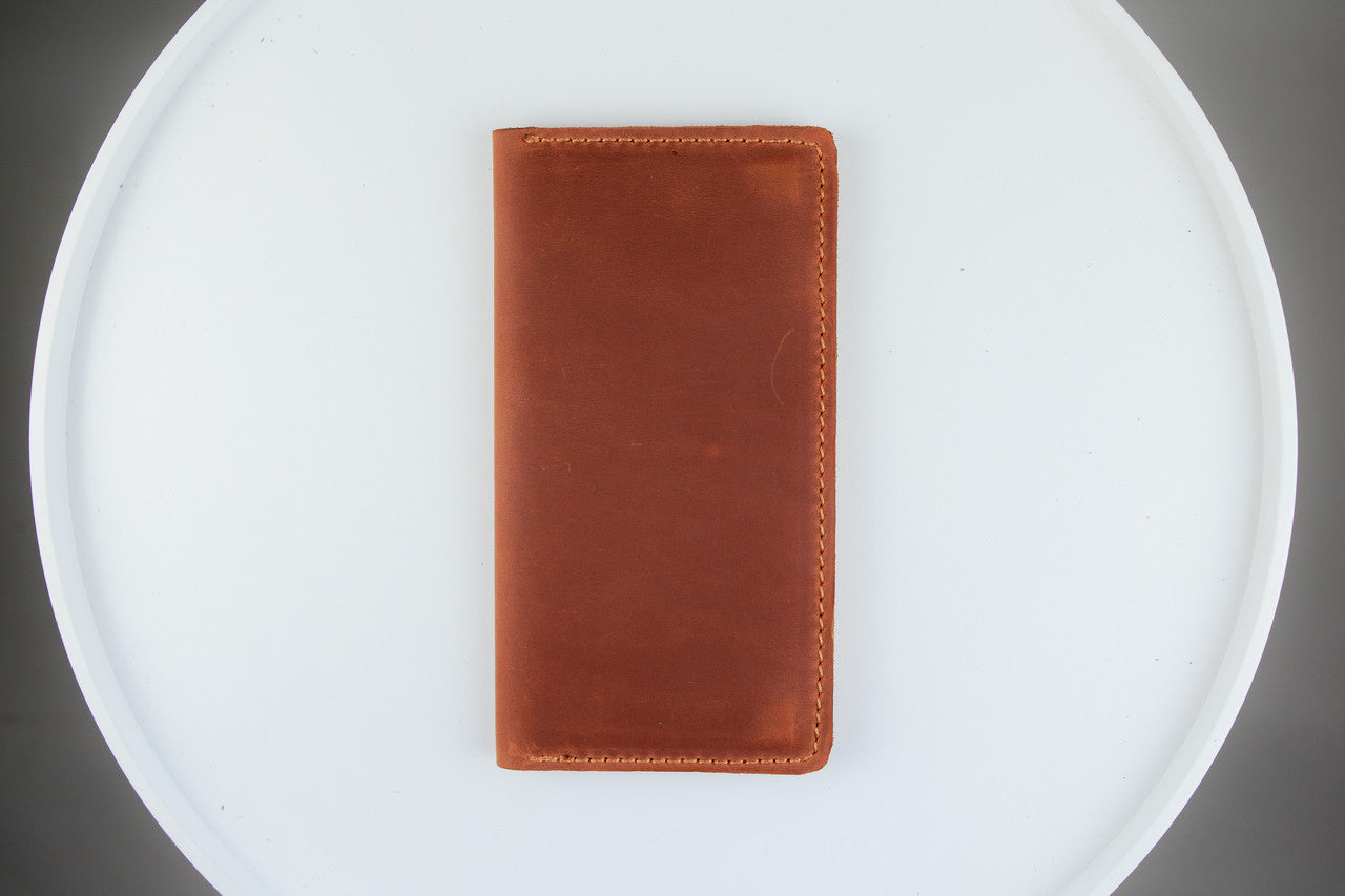 A brown leather wallet or card holder standing upright on a white circular tray against a dark gray background.