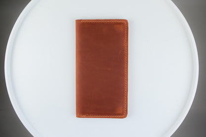 A brown leather wallet or card holder standing upright on a white circular tray against a dark gray background.