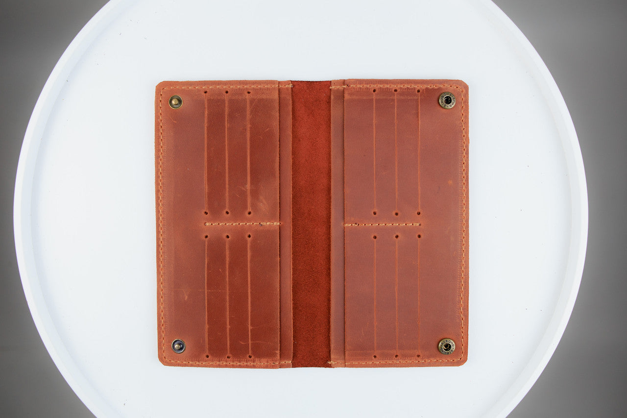 A brown leather card holder wallet shown open, displaying its interior card slots and suede-like center band, set against a white circular background.