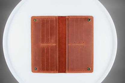 A brown leather card holder wallet shown open, displaying its interior card slots and suede-like center band, set against a white circular background.