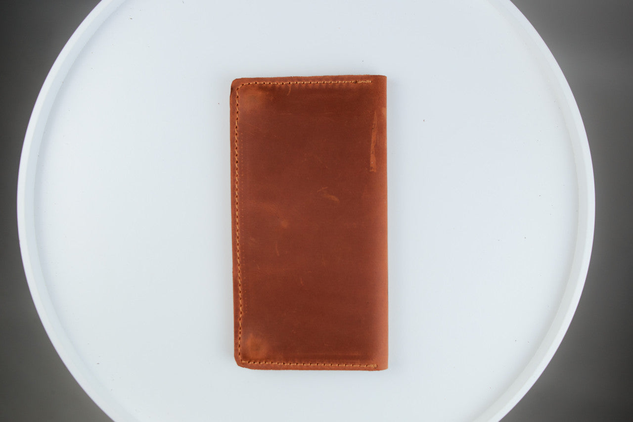 A brown leather card holder wallet with visible stitching, placed vertically on a white round tray against a dark gray background.