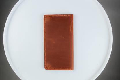 A brown leather card holder wallet with visible stitching, placed vertically on a white round tray against a dark gray background.