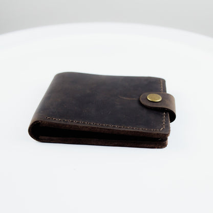 A dark brown leather bi-fold wallet with a snap-button closure, displayed on a clean white surface.