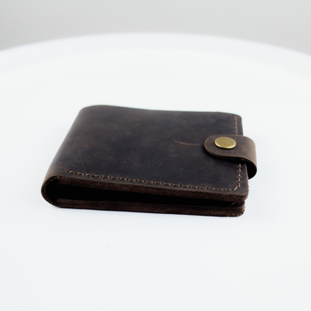 A dark brown leather bi-fold wallet with a snap-button closure, displayed on a clean white surface.